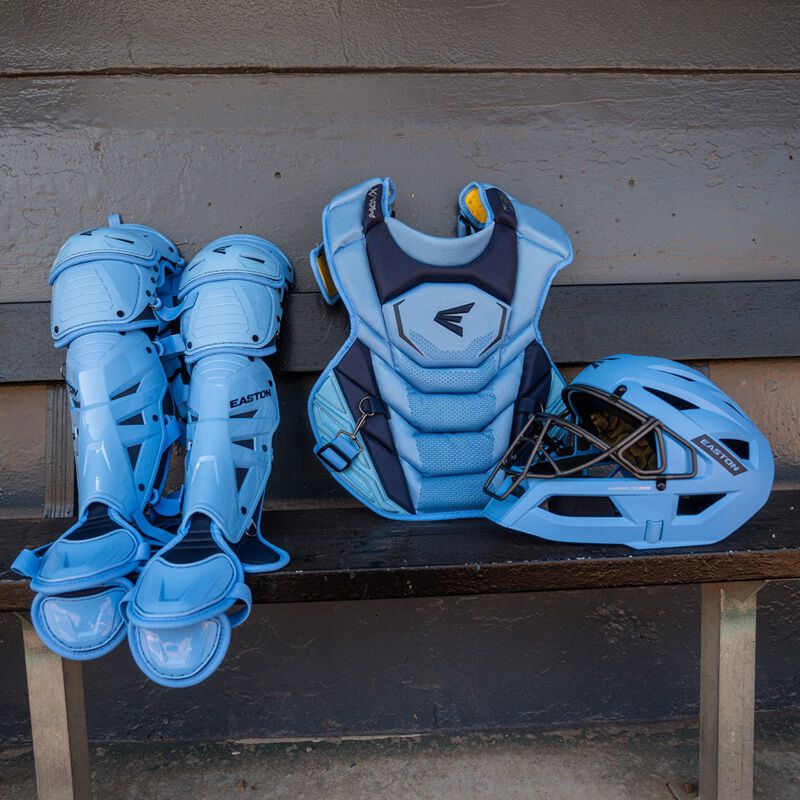 Light blue and navy Easton Mavrix catcher's set including leg guards, chest protector, and helmet displayed on a dugout bench