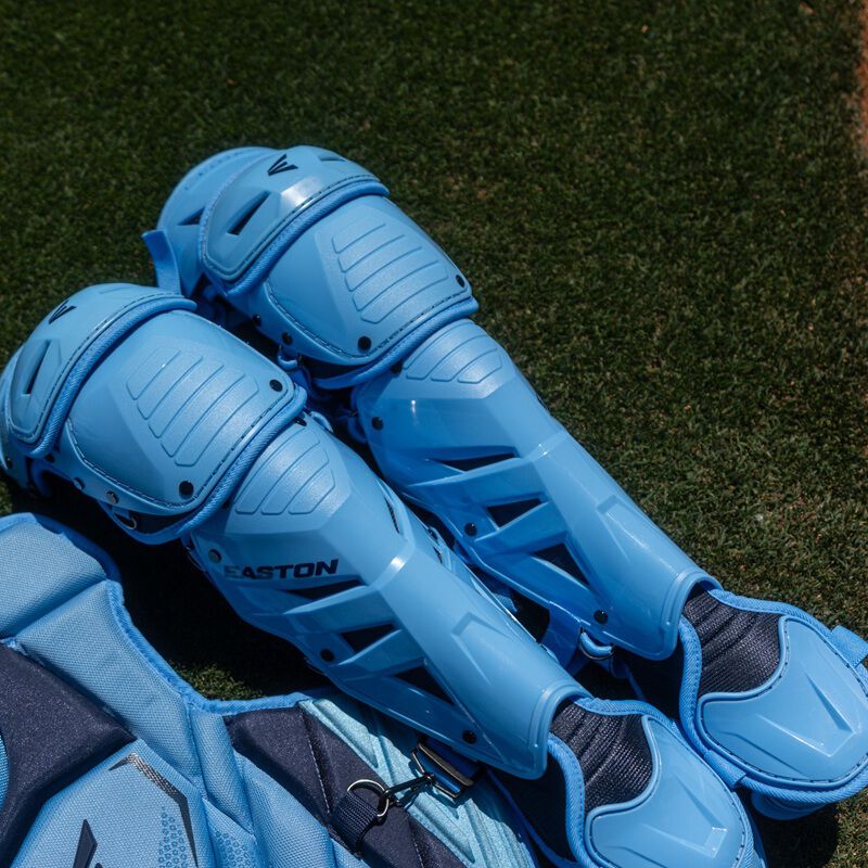 Light blue Easton Mavrix leg guards stacked on top of chest protector on artificial turf