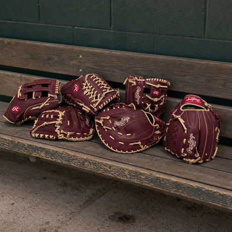 Maroon baseball gloves with gold stitching on a wooden bench against a green wall.